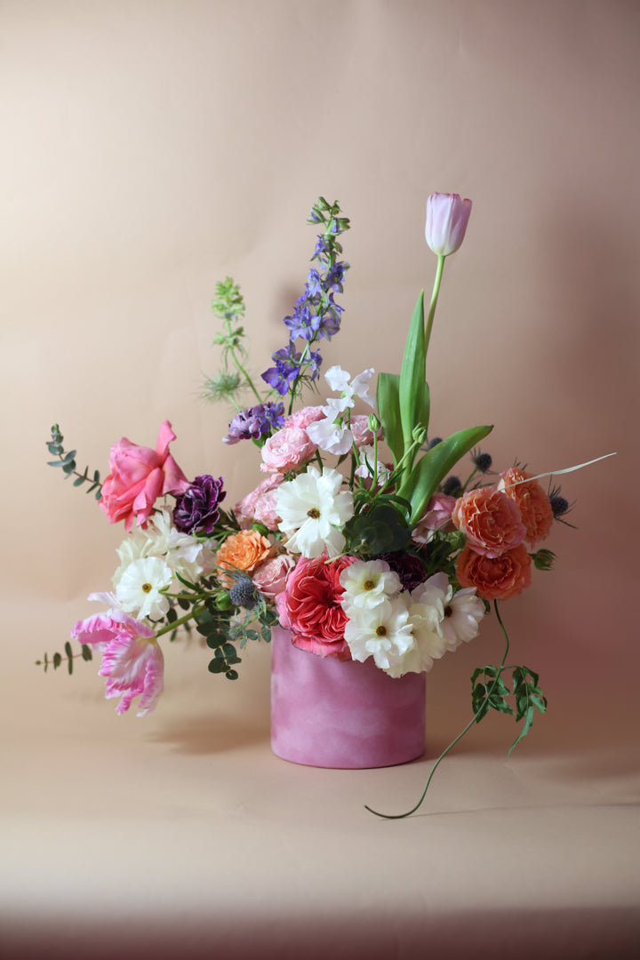 A vibrant arrangement of various flowers including garden roses and tulips, presented in a pink velvet box.