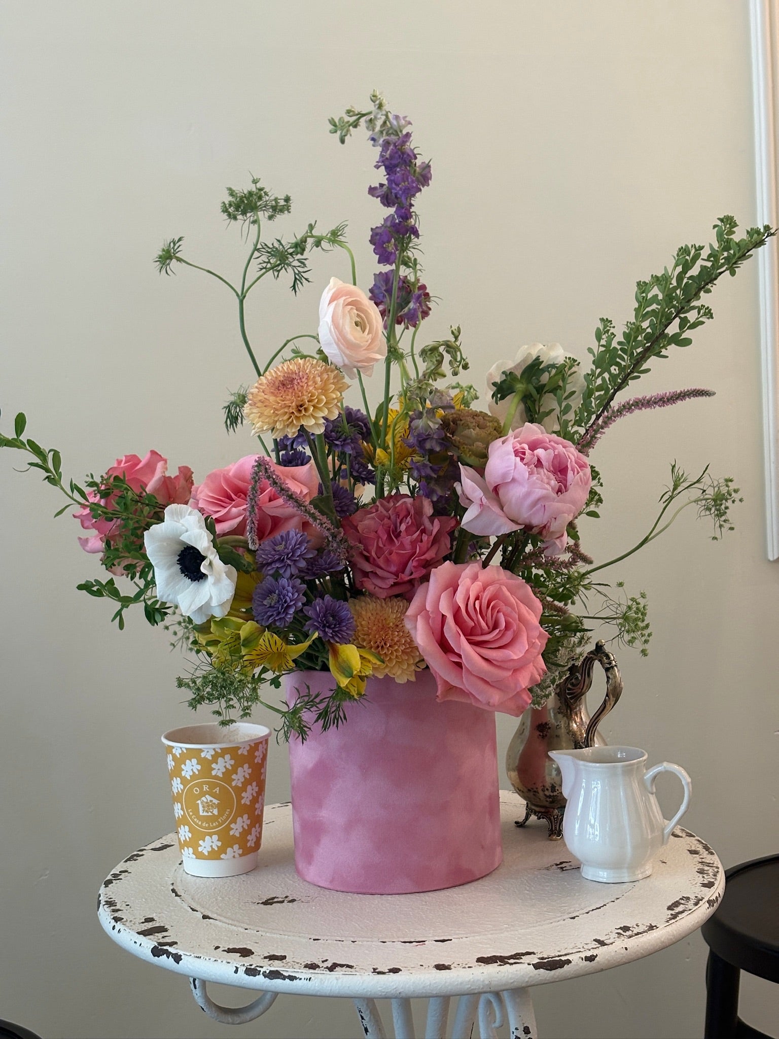 Bouquet of flowers in a pink vase on a small round table with a white background